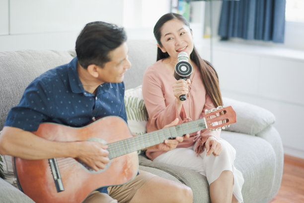 一对亚洲老人在养老院弹吉他唱歌。退休的男人和女人正在玩音乐，享受和微笑的感觉幸福坐在沙发上。图片下载