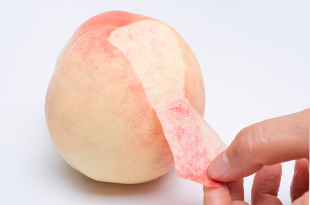 一只手正在撕桃子的薄皮。图片下载