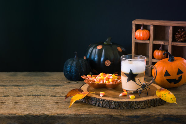 万圣节的概念，拿铁玛奇朵杯，糖果玉米和南瓜装饰在木桌上图片下载