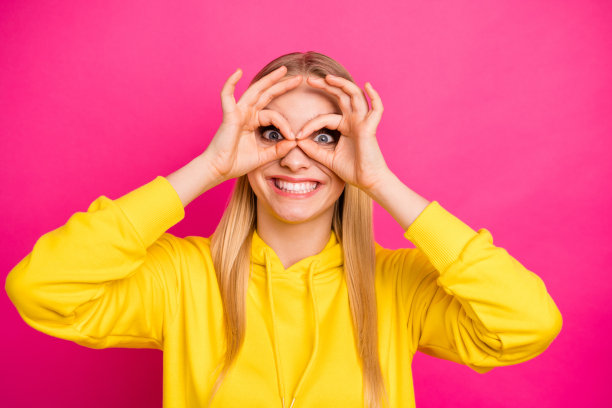 特写照片漂亮的女士看通过眼镜形状的手指穿黄色帽衫套头衫孤立的粉色背景图片下载