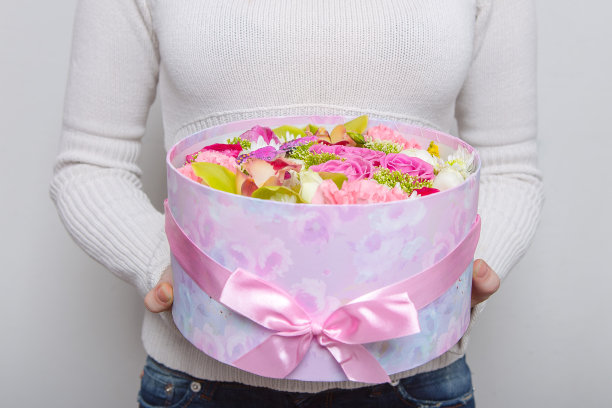 一个女人正拿着一个白色背景上美丽的花组成的盒子。图片下载