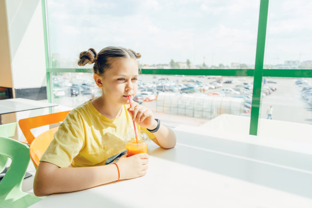 一个十几岁的女孩坐在咖啡馆里喝胡萝卜冰沙图片下载