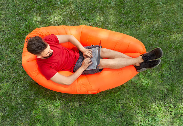 长着胡子的学生在空中沙发上摆弄电脑。图片下载