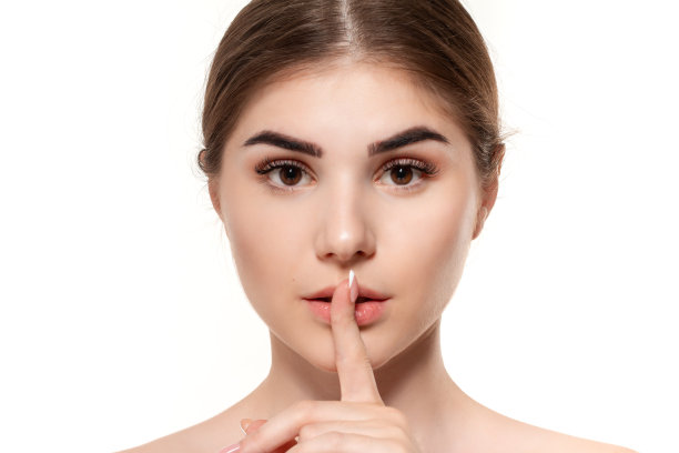 一个美丽的年轻女孩的特写肖像，在她的嘴附近的手指表达秘密孤立的想法在白色的背景。图片下载