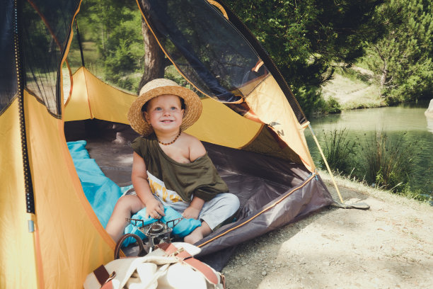 一个可爱的小男孩躲在帐篷里玩。快乐的孩子在户外玩露营。戴着草帽和太阳镜。图片下载