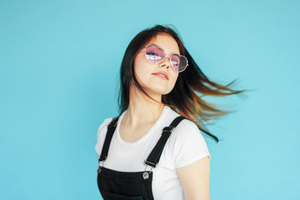 美丽快乐的女孩在眼镜与黑色长发在白色t恤孤立在蓝色背景，在运动图片下载