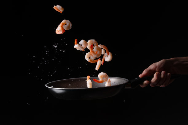 特写，海鲜，厨师在煎锅里煎虾。以黑色为背景进行设计，菜单、餐厅、东方料理、健康食品。水平的照片图片下载