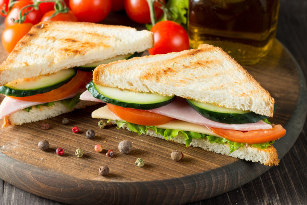 俱乐部三明治的特写照片。三明治与肉，火腿，意大利腊肠，沙拉，蔬菜，生菜，番茄，洋葱和芥末在新鲜的黑麦面包切片在木制背景。橄榄背景。图片下载
