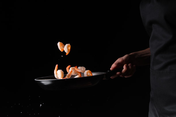 特写，海鲜，厨师在煎锅里煎虾。以黑色为背景进行设计，菜单、餐厅、东方料理、健康食品。水平的照片图片下载