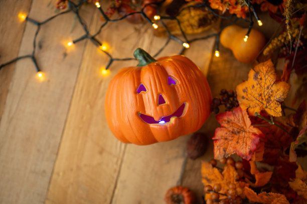 万圣节的南瓜与树叶在一个古老的木制桌子上发光的灯。从以上观点。副本的空间。秋的心情，和大气的照片。图片下载