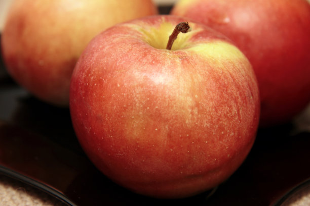 三个新鲜的红苹果放在桌子上的黑盘子里图片下载