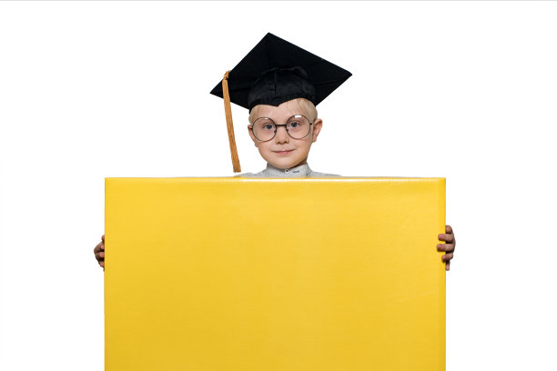 戴着学术帽和眼镜的金发男孩拿着一个大盒子。隔离。学校的概念图片下载