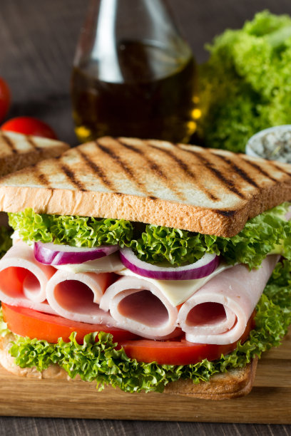俱乐部三明治的特写照片。三明治与肉，火腿，意大利腊肠，沙拉，蔬菜，生菜，番茄，洋葱和芥末在新鲜的黑麦面包切片在木制背景。橄榄背景。图片下载