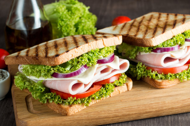 俱乐部三明治的特写照片。三明治与肉，火腿，意大利腊肠，沙拉，蔬菜，生菜，番茄，洋葱和芥末在新鲜的黑麦面包切片在木制背景。橄榄背景。图片下载