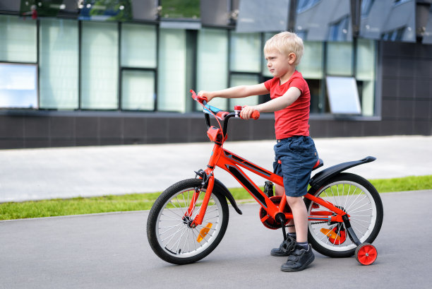 骑着儿童自行车的金发男孩。城市背景图片下载