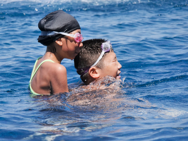 一个亚洲少年在阳光明媚的日子里背着他的妹妹在泳池里，生活方式的概念。图片下载