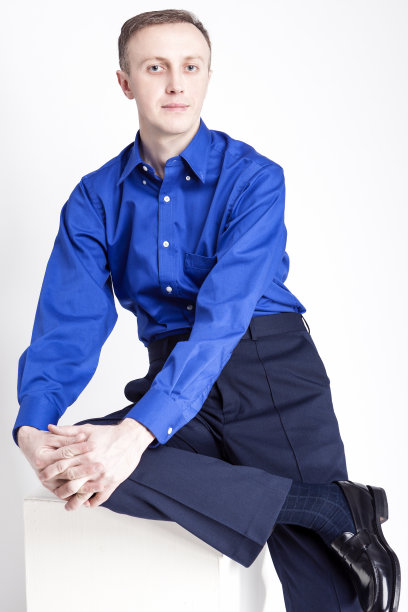 年轻的成年人的概念。帅气的白人男子的肖像与合手摆姿势在蓝色衬衫和深蓝色斜纹棉布对白色的背景。垂直的图像图片下载