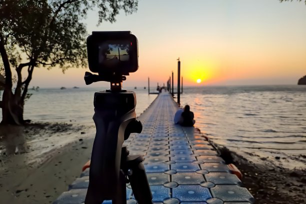 安装在三脚架上的摄像机拍摄码头上的小轿车和海底的日出。对焦相机图片下载