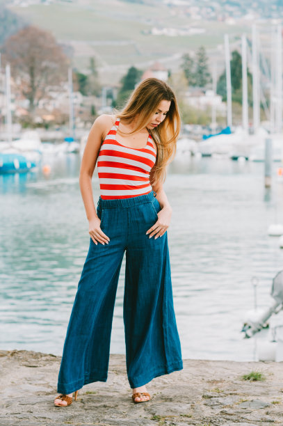 户外时尚肖像美丽的年轻女子摆姿势在湖边，穿着红白条纹背心和牛仔宽腿牛仔裤图片下载