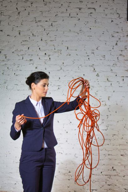 自信的年轻女商人看着白色砖墙上缠结的红色电缆图片下载