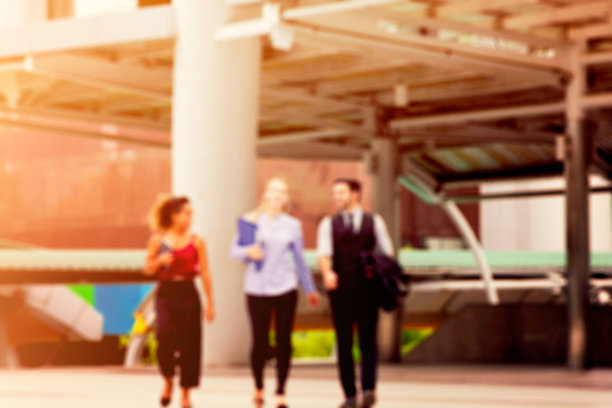 三名商务人士在建筑物外的灯光下行走和交谈的散焦照片图片下载