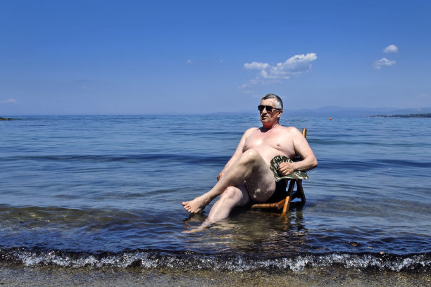 一位老人坐在海边的椅子上图片下载