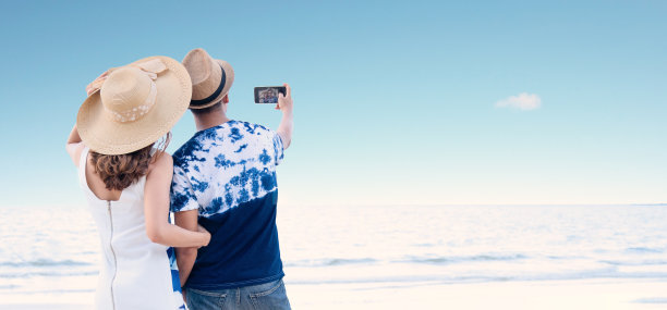 一对快乐的小情侣在海滩自拍。蜜月夫妇浪漫的爱情在海滩日落。在海边散步。一对年轻情侣在海滩上用智能手机自拍。图片下载