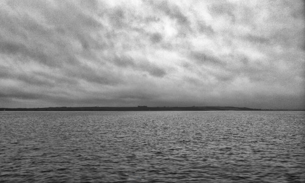 粒状的单色图像，一个平坦平静的海与黑暗的云反映在水与陆地在地平线上图片下载