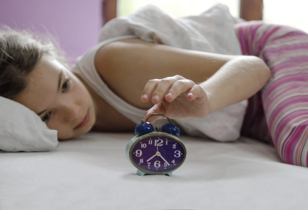 小女孩躺在床上，闹钟响了。新的一天开始了图片下载