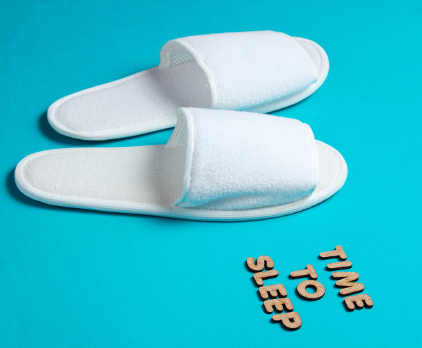 时间睡觉。蓝色背景下的白色旅馆拖鞋图片下载