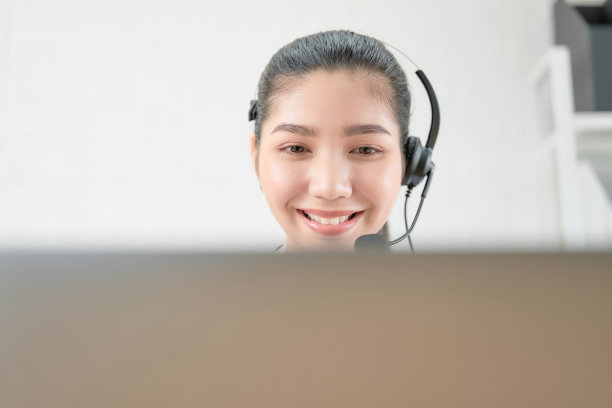 微笑的亚洲女顾问戴着客户支持电话接线员的麦克风在工作场所。图片下载