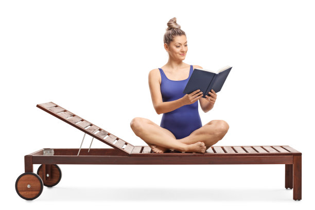 年轻的金发女郎穿着泳衣在躺椅上看书图片下载