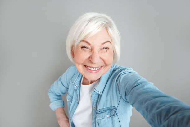 资深女子在牛仔夹克工作室孤立在灰色墙壁上自拍照片图片下载