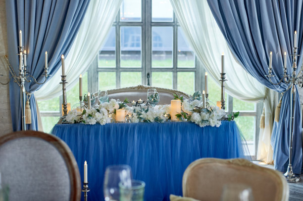 婚礼桌上装饰着白色的鲜花，蜡烛。有靠垫的软沙发，大窗户。蓝白相间的图片下载