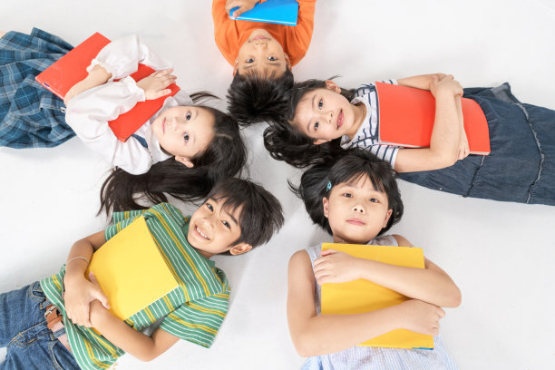 孩子们躺在白色的地板上看书，头挨着头，围成一圈，幼儿园图书馆，幼儿园教育理念图片下载