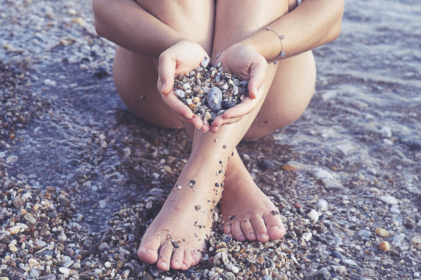 一位年轻女子手握希腊海滩上美丽多彩的鹅卵石。图片下载