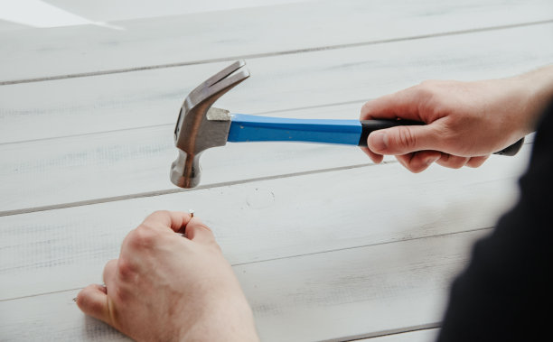 一个男人用锤子把钉子钉到木板上。DIY、新事物翻新的概念。图片下载