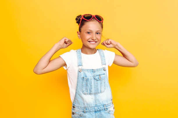 快乐的少女微笑和摆姿势，显示胜利和成功的黄色背景图片下载
