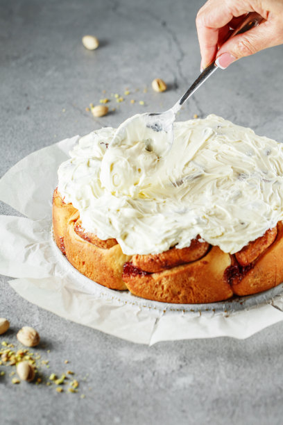 肉桂面包。奶油芝士，奶油和红糖卷在灰色的背景。肉桂卷配覆盆子和开心果。用奶油装饰蛋糕的过程。把手放在照片上图片下载