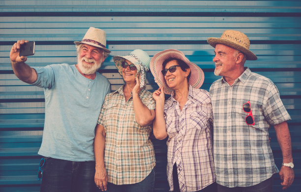 快乐的四名老人在友谊站在一堵墙微笑和使用电话。愉快和放松的面孔。图片下载