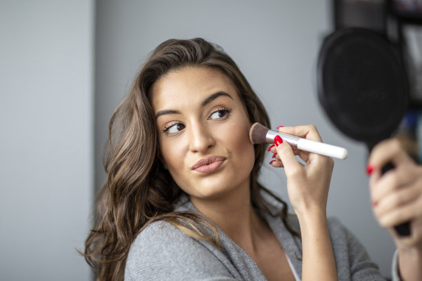 女人手拿刷子和镜子坐在沙发上化妆图片下载