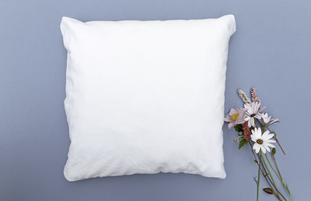 空白的白色垫子模板在蓝色的背景与野花的右边-完美的枕头垫子电子商务模型图片下载