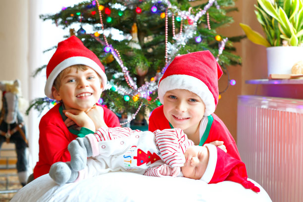 刚出生的女婴和两个哥哥在圣诞树旁戴着圣诞帽的男孩图片下载