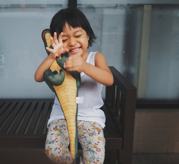模糊的照片复古风格的儿童亚洲女孩愉快地拥抱恐龙娃娃。图片下载