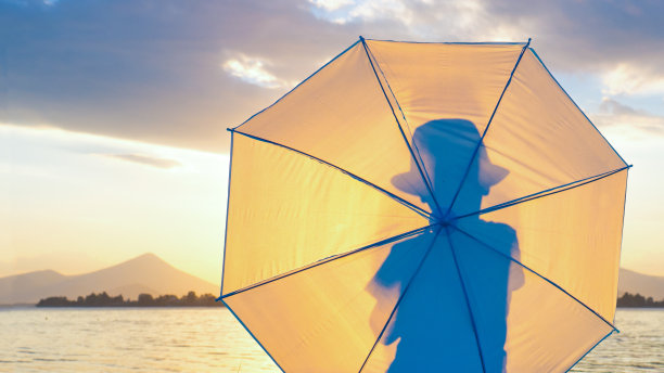 拍摄背景。时髦的潮人，小男孩戴着帽子和雨伞在海边。一个人的背影剪影，以日落日出为背景，背光效果，画面变暗。本空间图片下载
