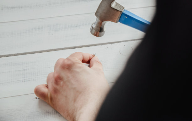 一个男人用锤子把钉子钉到木板上。DIY、新事物翻新的概念。图片下载