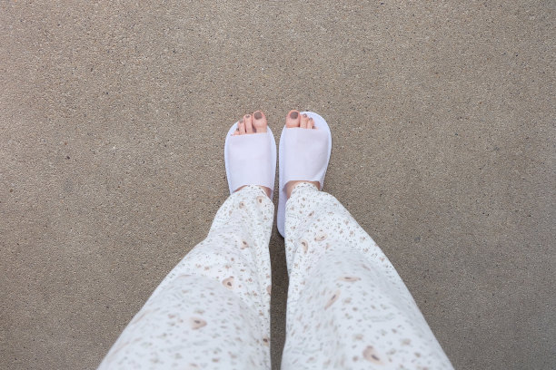 混凝土背景下的自拍拖鞋，俯视图。漂亮的年轻女子，穿着白色拖鞋和裤子。清暖的家凉鞋。图片下载