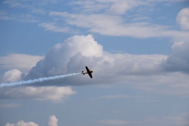 一架小型黄色客机在多云的夏季天空中快速而动态地飞行，并在机后产生一些烟雾，在高空向预定的目的地飞行图片下载
