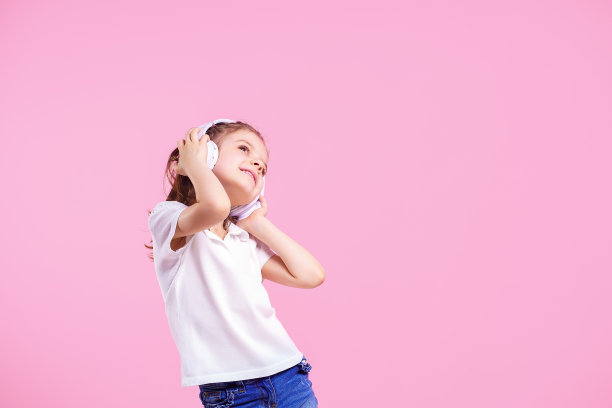 女孩戴着耳机在听粉色背景的音乐。可爱的孩子享受着欢快的舞曲，闭上眼睛，微笑着在工作室背景墙上摆姿势图片下载