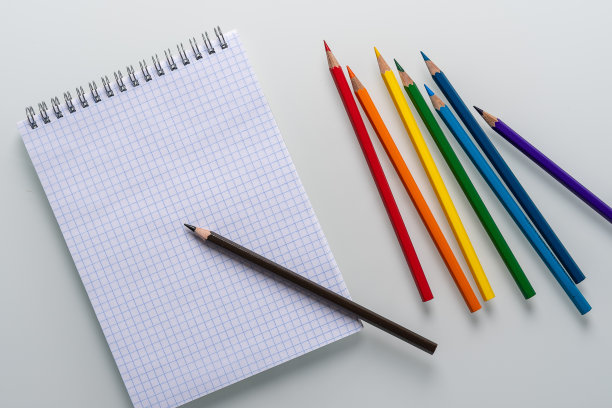 干净的记事本在一个笼子里与一支铅笔躺在它和彩虹色铅笔在一个白色的背景顶视图拷贝空间图片下载